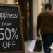 Man of color with shopping bags walking past a chalkboard sign saying “Happiness: now 50% off”